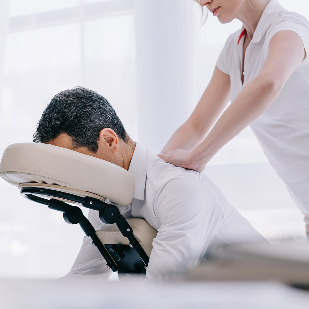 Masseuse doing seated back massage for businessman at office